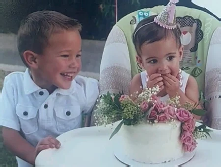Two little ones laughing at a first birthday cake decorated with pink flowers