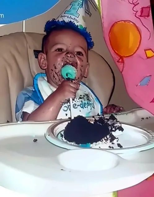 A one-year-old with chocolate cake on his face in a high chair