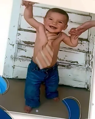A one-year-old standing and smiling while holding a grown-up's hands